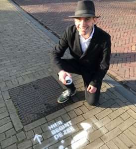 Wethouder Paul Hofman van Bronckhorst spuit het logo 'Hier begint de zee'bij een straatput met biologisch afbreekbare verf