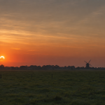 Afbeelding van de gedeeltelijke zonsverduistering boven een landelijk gebied.